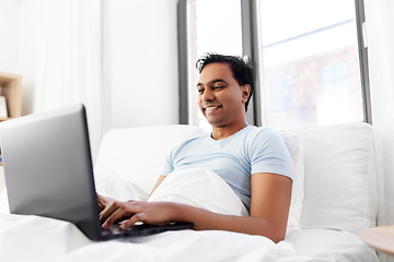 Image showing happy indian man with laptop in bed at home