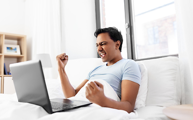 Image showing happy indian man with laptop in bed at home