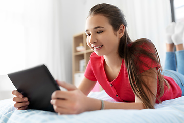 Image showing smiling girl with tablet pc lying on bed at home