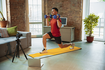 Image showing Young caucasian man training at home during quarantine of coronavirus outbreak, doing exercises of fitness, aerobic. Staying sportive during insulation.