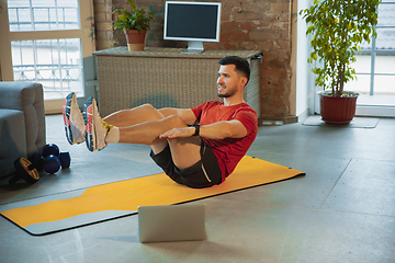 Image showing Young caucasian man training at home during quarantine of coronavirus outbreak, doing exercises of fitness, aerobic. Staying sportive during insulation.