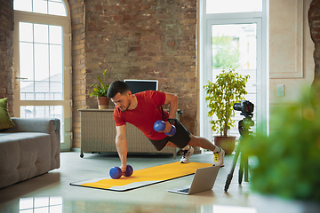 Image showing Young caucasian man training at home during quarantine of coronavirus outbreak, doing exercises of fitness, aerobic. Staying sportive during insulation.