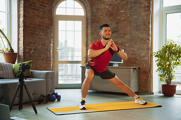 Image showing Young caucasian man training at home during quarantine of coronavirus outbreak, doing exercises of fitness, aerobic. Staying sportive during insulation.