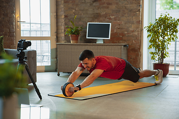 Image showing Young caucasian man training at home during quarantine of coronavirus outbreak, doing exercises of fitness, aerobic. Staying sportive during insulation.