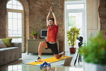 Image showing Young caucasian man training at home during quarantine of coronavirus outbreak, doing exercises of fitness, aerobic. Staying sportive during insulation.