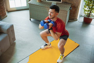 Image showing Young caucasian man training at home during quarantine of coronavirus outbreak, doing exercises of fitness, aerobic. Staying sportive during insulation.