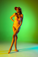 Image showing Beautiful girl in fashionable swimsuit isolated on gradient studio background in neon light. Summer, resort, fashion and weekend concept