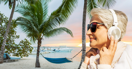 Image showing old woman in headphones listens to music on beach