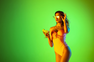 Image showing Beautiful girl in fashionable swimsuit isolated on gradient studio background in neon light. Summer, resort, fashion and weekend concept