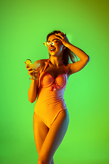 Image showing Beautiful girl in fashionable swimsuit isolated on gradient studio background in neon light. Summer, resort, fashion and weekend concept