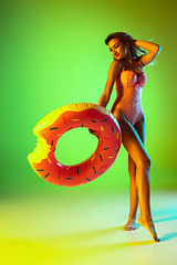 Image showing Beautiful girl in fashionable swimsuit isolated on gradient studio background in neon light. Summer, resort, fashion and weekend concept