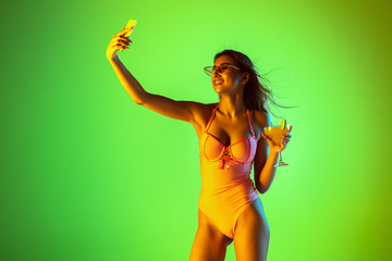 Image showing Beautiful girl in fashionable swimsuit isolated on gradient studio background in neon light. Summer, resort, fashion and weekend concept