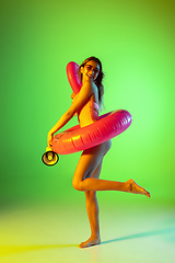 Image showing Beautiful girl in fashionable swimsuit isolated on gradient studio background in neon light. Summer, resort, fashion and weekend concept