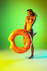 Image showing Beautiful girl in fashionable swimsuit isolated on gradient studio background in neon light. Summer, resort, fashion and weekend concept