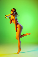 Image showing Beautiful girl in fashionable swimsuit isolated on gradient studio background in neon light. Summer, resort, fashion and weekend concept