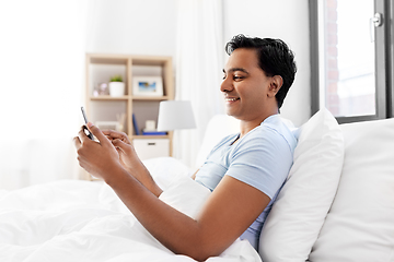 Image showing happy indian man with smartphone in bed at home