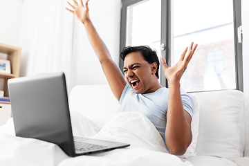 Image showing happy indian man with laptop in bed at home