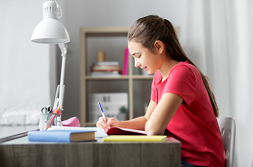 Image showing student girl with book writing to notebook at home