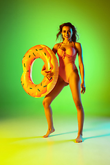 Image showing Beautiful girl in fashionable swimsuit isolated on gradient studio background in neon light. Summer, resort, fashion and weekend concept