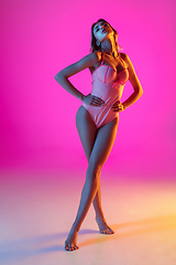 Image showing Beautiful girl in fashionable swimsuit isolated on gradient studio background in neon light. Summer, resort, fashion and weekend concept