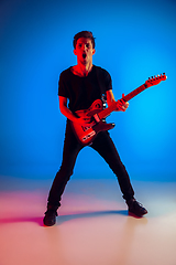 Image showing Young caucasian musician playing guitar in neon light on blue background, inspired