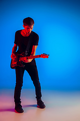 Image showing Young caucasian musician playing guitar in neon light on blue background, inspired