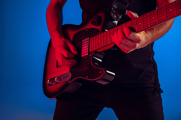 Image showing Young caucasian musician playing guitar in neon light on blue background, inspired