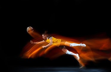 Image showing Young female volleyball player isolated on black studio background. Woman in sport\'s equipment training and practicing with fire shadow behind her