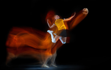 Image showing Young female volleyball player isolated on black studio background. Woman in sport\'s equipment training and practicing with fire shadow behind her