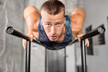 Image showing man doing push-ups on parallel bars in gym