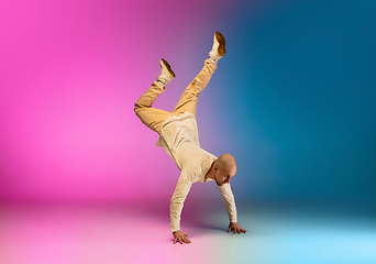 Image showing Stylish sportive caucasian man dancing hip-hop on colorful gradient background at dance hall in neon light.