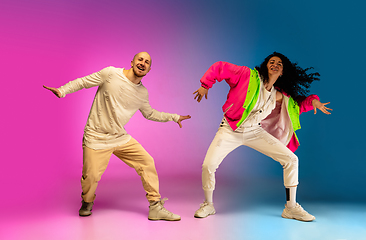 Image showing Stylish sportive caucasian couple dancing hip-hop on colorful gradient background at dance hall in neon light.