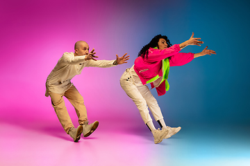 Image showing Stylish sportive caucasian couple dancing hip-hop on colorful gradient background at dance hall in neon light.