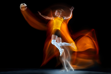 Image showing Young female volleyball player isolated on black studio background. Woman in sport\'s equipment training and practicing with fire shadow behind her