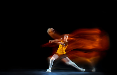 Image showing Young female volleyball player isolated on black studio background. Woman in sport\'s equipment training and practicing with fire shadow behind her