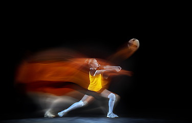 Image showing Young female volleyball player isolated on black studio background. Woman in sport\'s equipment training and practicing with fire shadow behind her