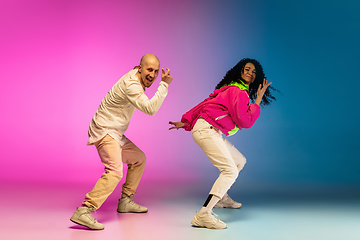 Image showing Stylish sportive caucasian couple dancing hip-hop on colorful gradient background at dance hall in neon light.