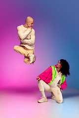 Image showing Stylish sportive caucasian couple dancing hip-hop on colorful gradient background at dance hall in neon light.