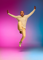 Image showing Stylish sportive caucasian man dancing hip-hop on colorful gradient background at dance hall in neon light.