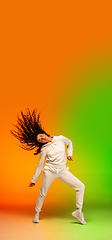 Image showing Stylish sportive caucasian woman dancing hip-hop on colorful gradient background at dance hall in neon light.