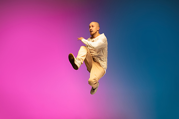 Image showing Stylish sportive caucasian man dancing hip-hop on colorful gradient background at dance hall in neon light.