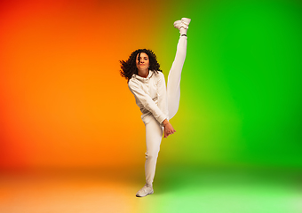 Image showing Stylish sportive caucasian woman dancing hip-hop on colorful gradient background at dance hall in neon light.