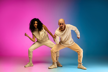 Image showing Stylish sportive caucasian couple dancing hip-hop on colorful gradient background at dance hall in neon light.