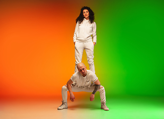 Image showing Stylish sportive caucasian couple dancing hip-hop on colorful gradient background at dance hall in neon light.