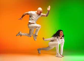 Image showing Stylish sportive caucasian couple dancing hip-hop on colorful gradient background at dance hall in neon light.