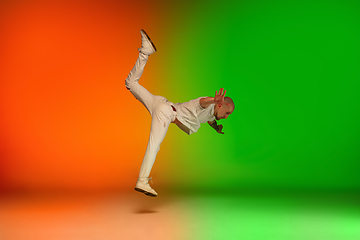 Image showing Stylish sportive caucasian man dancing hip-hop on colorful gradient background at dance hall in neon light.