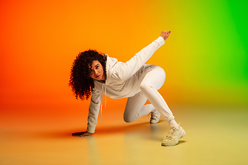 Image showing Stylish sportive caucasian woman dancing hip-hop on colorful gradient background at dance hall in neon light.
