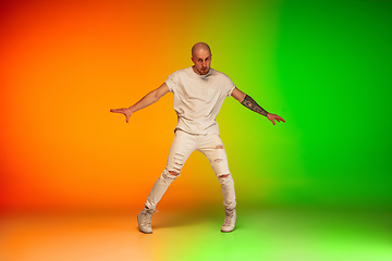 Image showing Stylish sportive caucasian man dancing hip-hop on colorful gradient background at dance hall in neon light.
