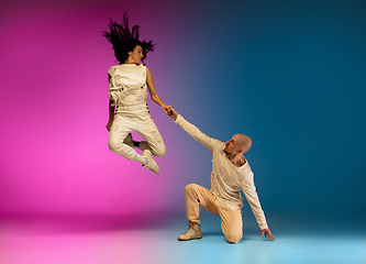 Image showing Stylish sportive caucasian couple dancing hip-hop on colorful gradient background at dance hall in neon light.