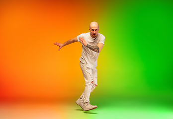 Image showing Stylish sportive caucasian man dancing hip-hop on colorful gradient background at dance hall in neon light.